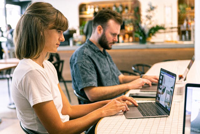 A man and woman sitting at a table with laptops, showcasing their expertise while maintaining a balanced approach