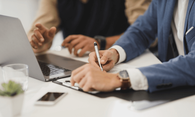 Two people at a table with a laptop and pen, discussing Marketing Automation strategy