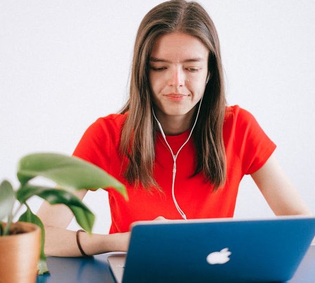 A woman wearing headphones sits at a desk, focused on her laptop.